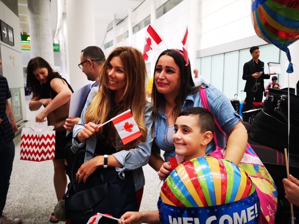 A family is greeted by new colleagues from Paramount Fine Foods in Toronto. The chef and his family arrived from displacement under Canada’s Economic Mobility Pathways Project. 